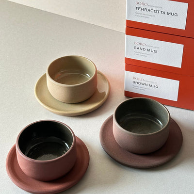 Three ceramic mugs in different colors with packaging on a light background