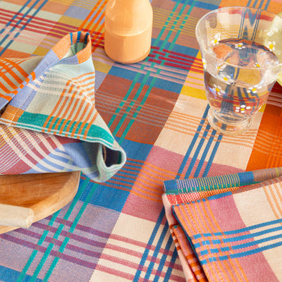 Colorful plaid tablecloth with a wooden vase holding flowers and a glass of water on a checkered tablecloth.