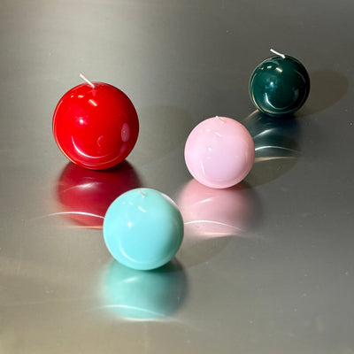 Four colorful spherical candles on a reflective surface