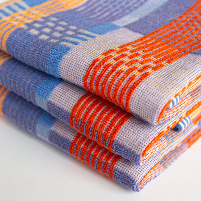multicoloured tea towel. mix of flat weave and terry cloth, in red, blue, orange and yellow yarns. a stack of 3 tea towels