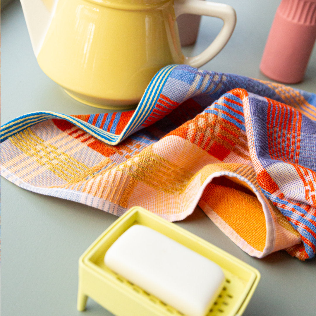multicoloured tea towel. mix of flat weave and terry cloth, in red, blue, orange and yellow yarns. in use in the kitchen, casually laid on the counter