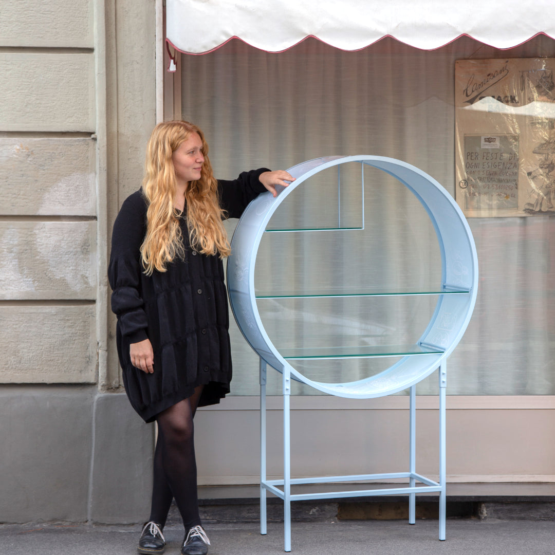 Portrait of furniture designer Liselotte Kirsch with her shelving unit in front of a store front