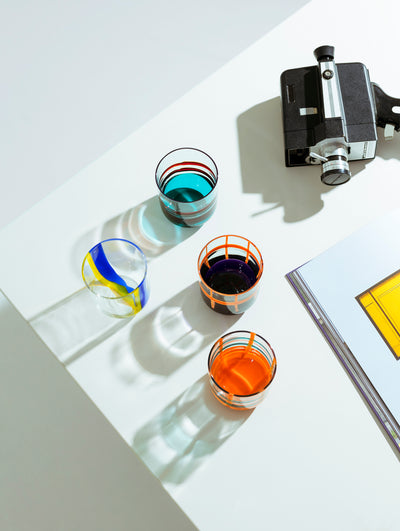 A collection of colorful, mouth-blown glasses with bold, graphic lines, displayed on a white table.