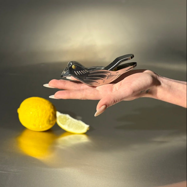 Hand holding a lemon squeezer with lemons on a reflective surface
