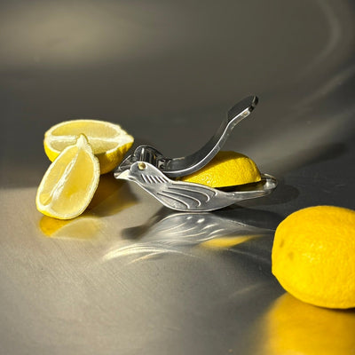 Metal lemon squeezer with lemons on a reflective surface