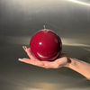 Hand holding a red spherical object against a reflective silver background