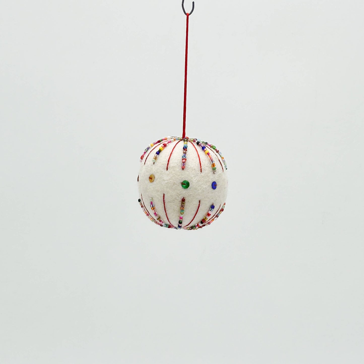 Decorative spherical ornament with colorful beads hanging on a red string against a light gray background
