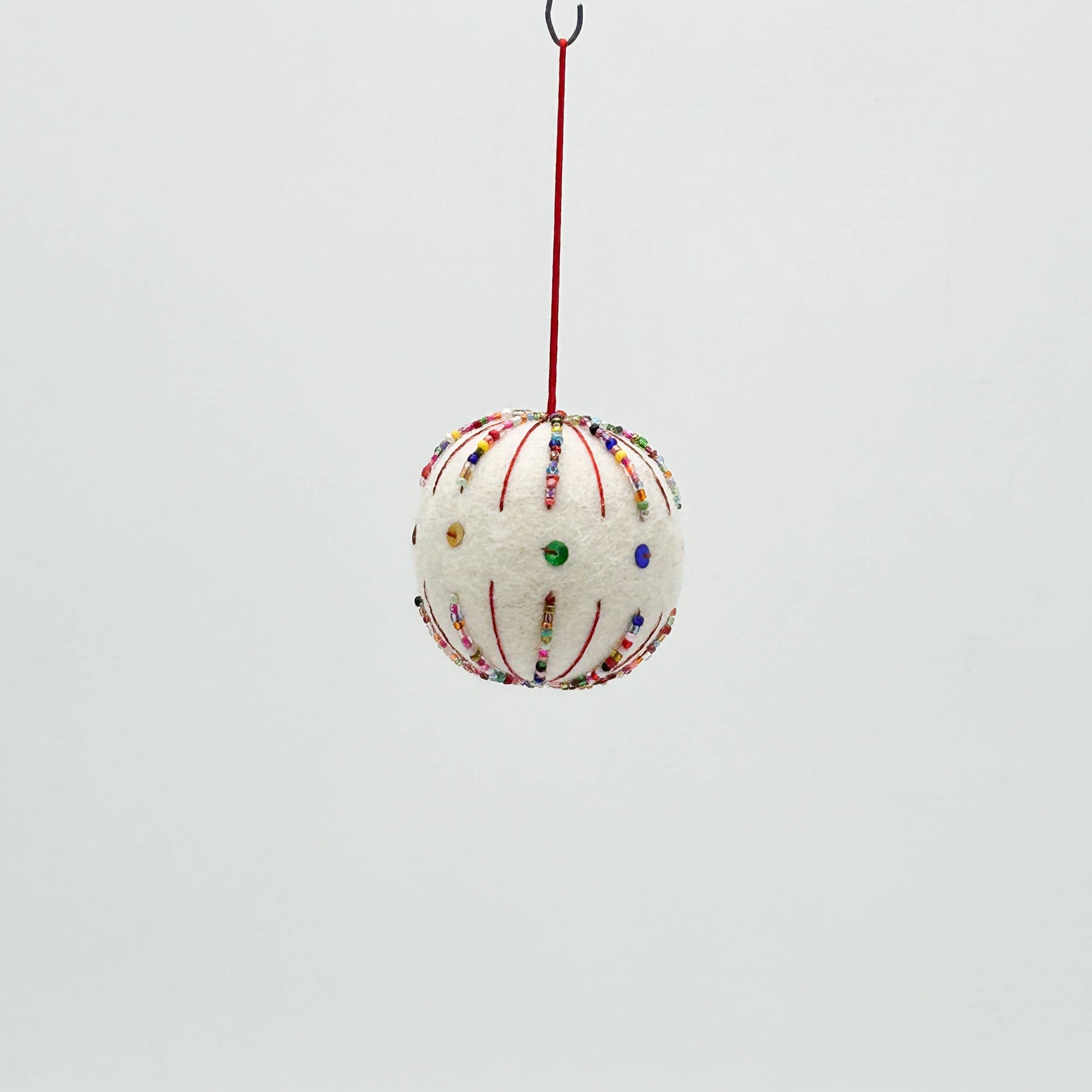 Decorative spherical ornament with colorful beads hanging on a red string against a light gray background
