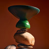 Two stacked stones with a green and brown object balanced on top against a brown background