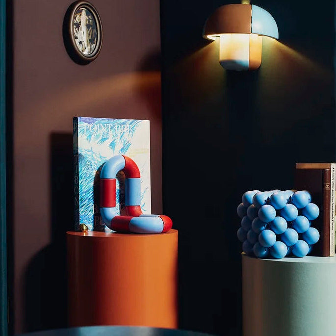 Decorative items on cylindrical stands against a dark wall with a clock.
