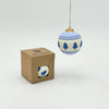 Decorative ball ornament with tree pattern hanging above a cardboard box on a white background