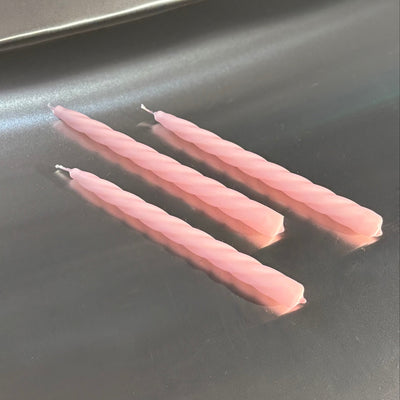 Three pink candles on a reflective metal surface