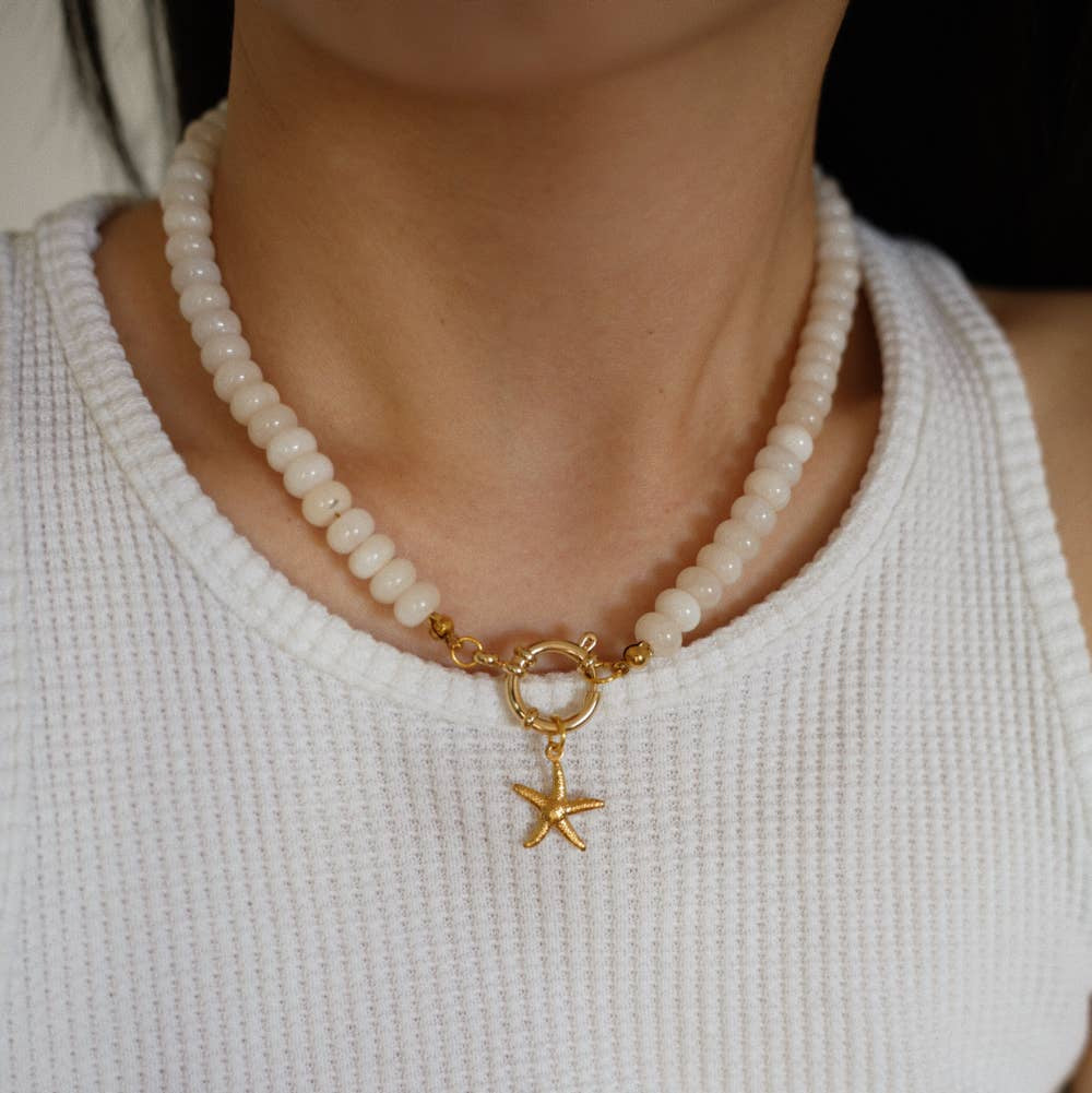 beaded necklace with a gold clasp and starfish charm worn by a person in a white top.