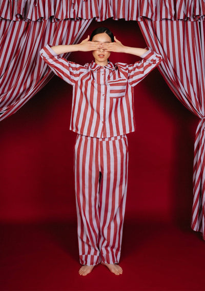Person wearing red and white striped pajamas standing in front of red and white striped curtains.