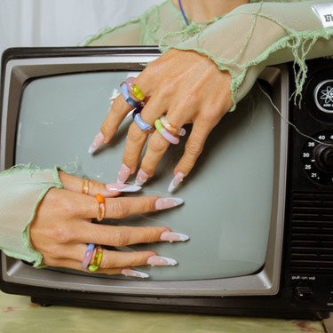 Vintage television with hands wearing colorful rings on a white background
