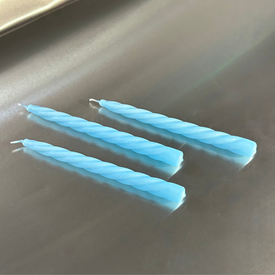 Three blue twisted candles on a reflective surface