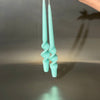 Turquoise candles held by a hand against a reflective surface with a dark background