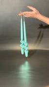 Turquoise candles held by a hand against a reflective surface with a dark background