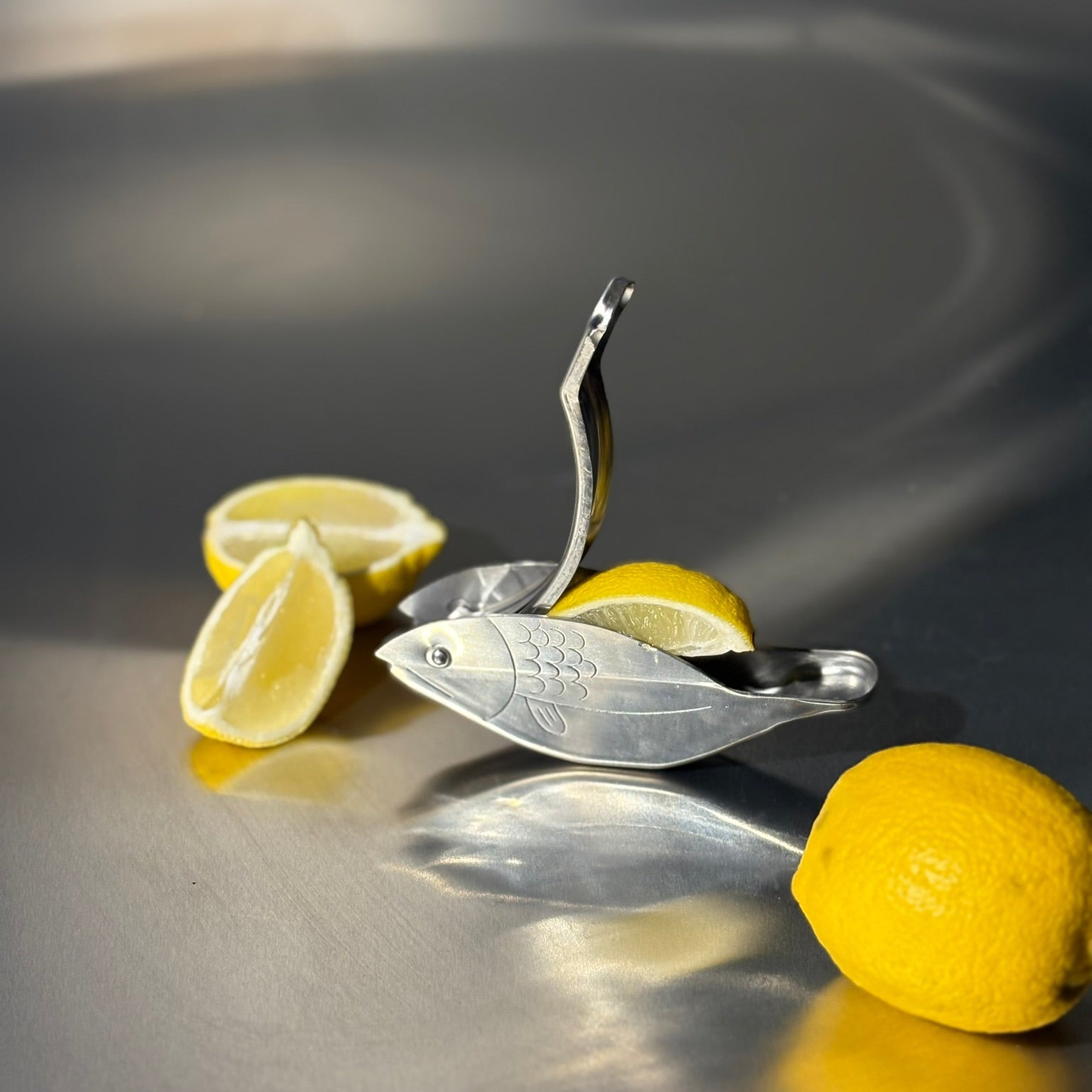Metal lemon squeezer with lemons on a reflective surface