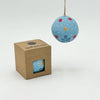 Blue decorative ball with colorful spots hanging above a cardboard box on a white background