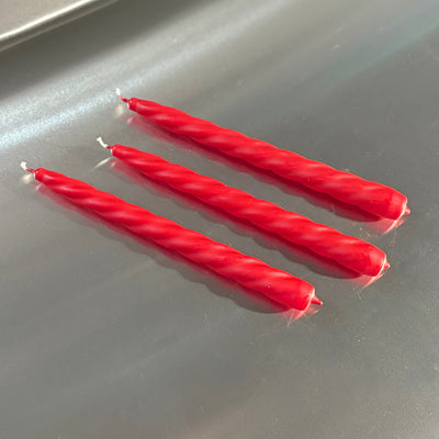 Three red twisted candles on a metallic surface