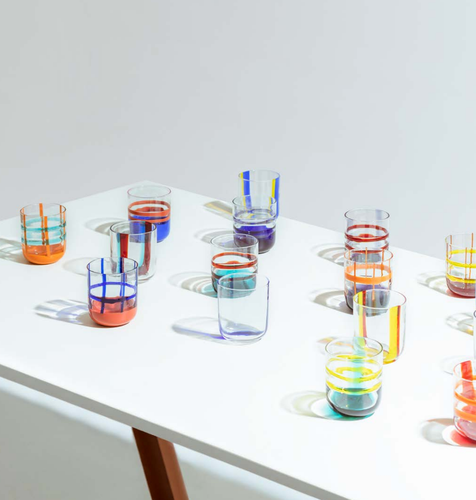 A collection of colorful, mouth-blown glasses with bold, graphic lines, displayed on a white table.