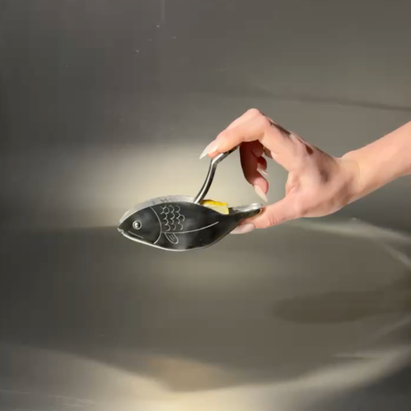 lemons squeezer - fish shaped, stainless steel, being squeezed by a female hand, on metal background