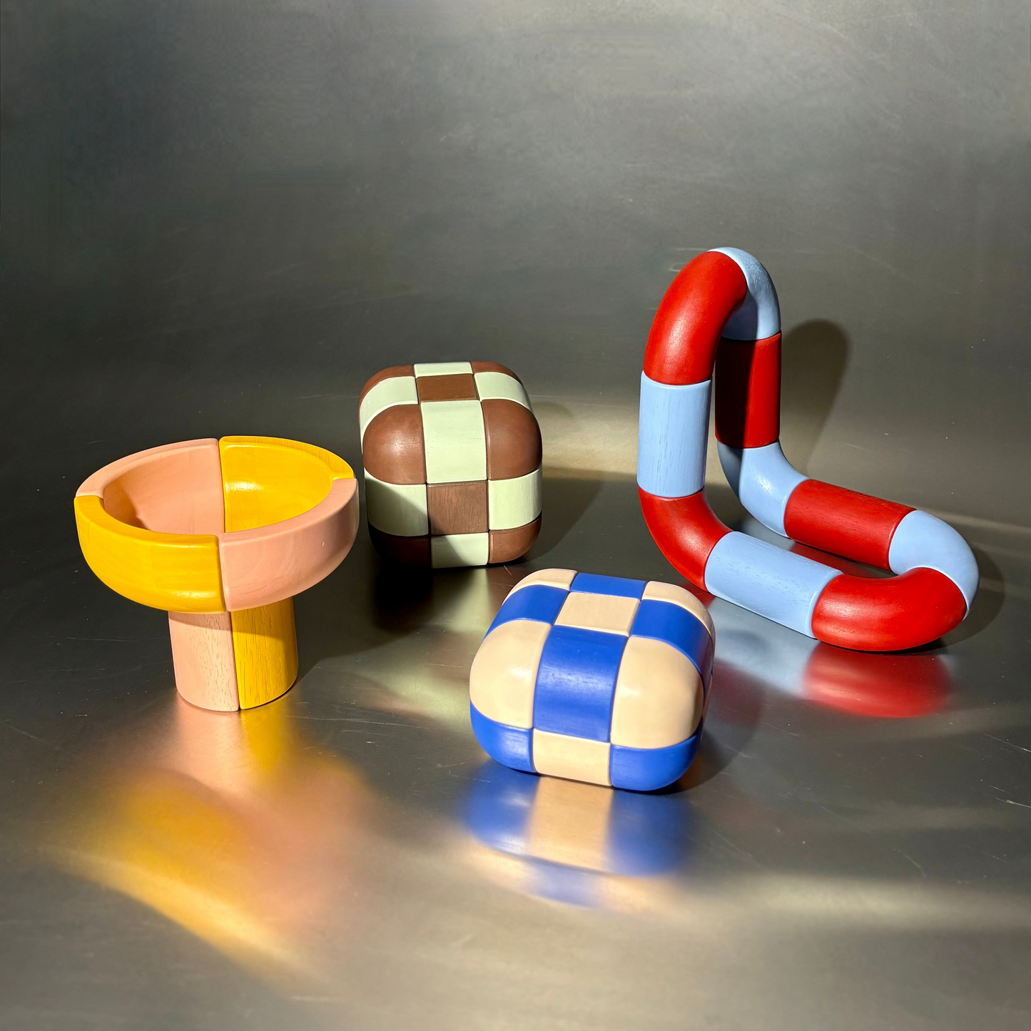 Colorful geometric sculptures on a reflective surface with a gray background