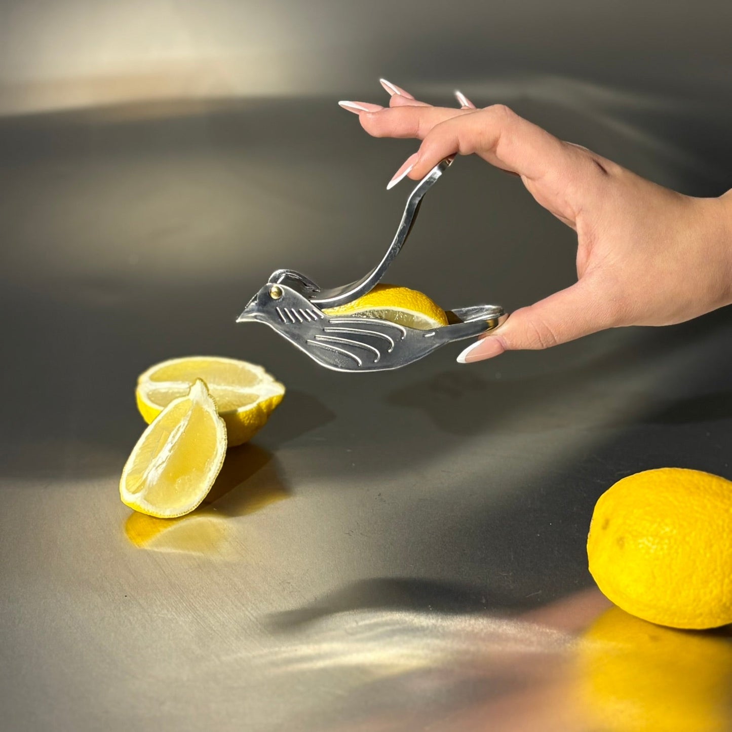 Hand using a lemon squeezer with lemons on a reflective surface