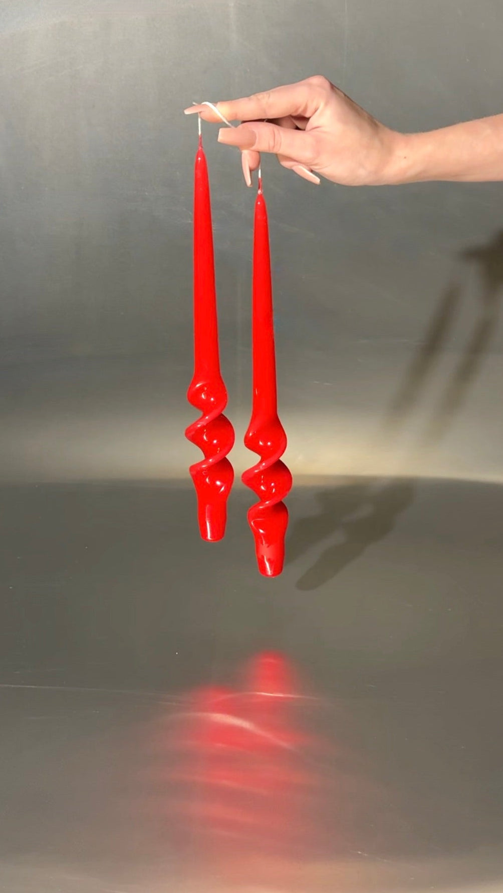 Red candlesticks held by a hand against a reflective gray background