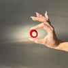 Hand holding a red ring against a neutral background