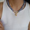 Person wearing a blue beaded necklace with a gold clasp on a white sleeveless top.
