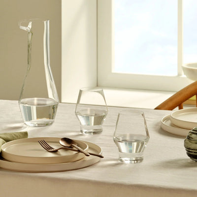 set of 2 beak glasses by tomas kral on a clean, beige coloured dining table, paired with the beak carafe and simple beige dinnerware