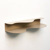 side view of blob shaped curvy shelf in beige against a white wall