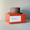 Brown mug with a white label on an orange box against a light gray background