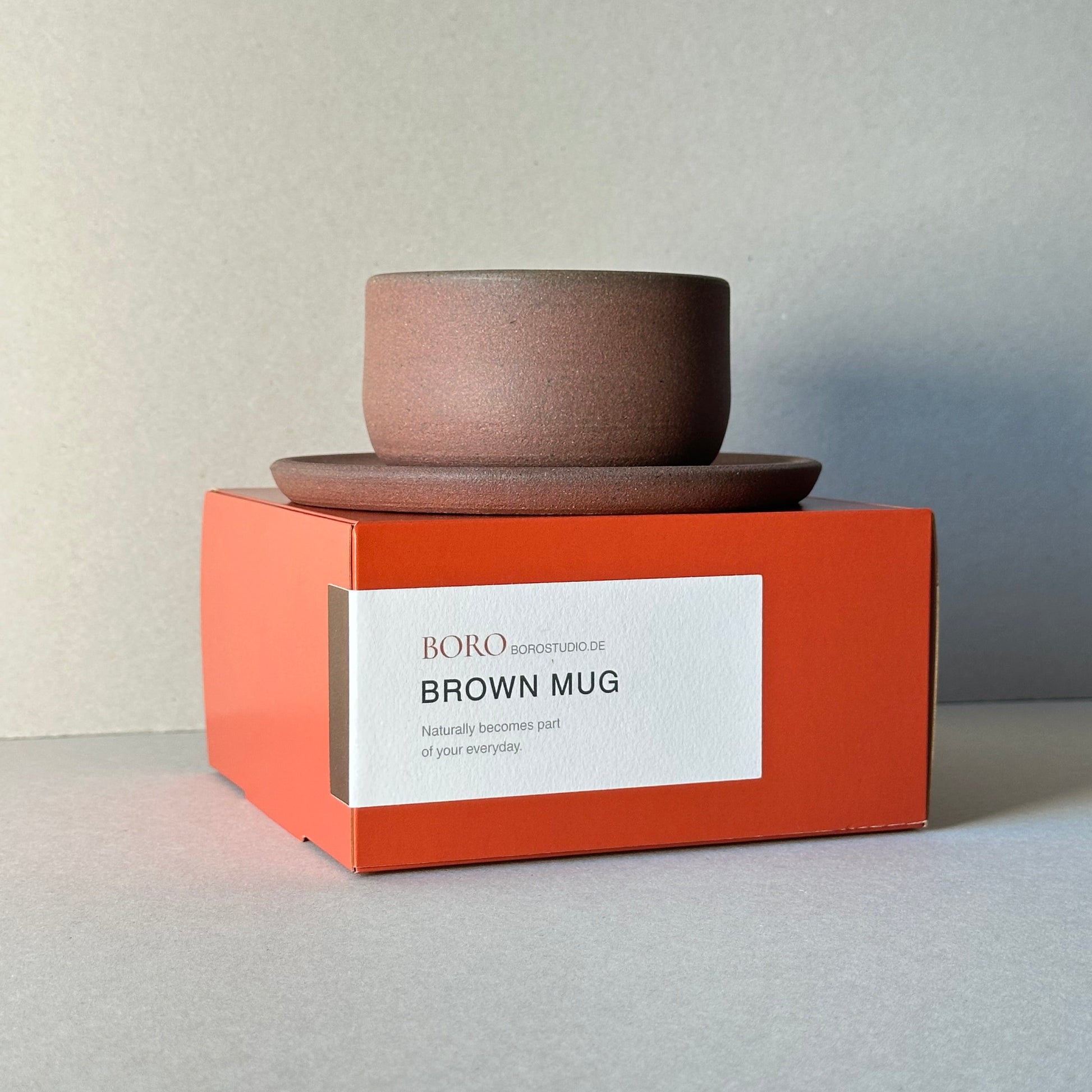 Brown mug with a white label on an orange box against a light gray background