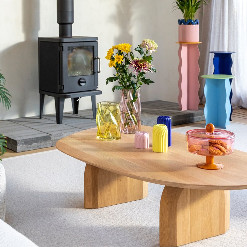 a decorated coffee table in the middle of a living room, decorated with brightly coloured vases, candle holders and cake stand