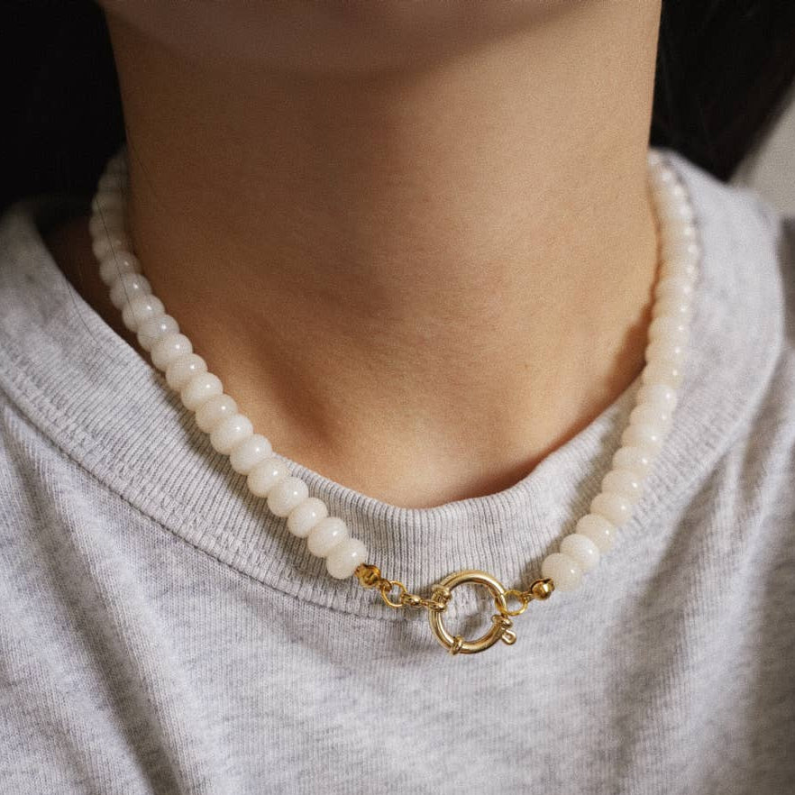 beaded necklace with a gold clasp worn by a person wearing a gray shirt.