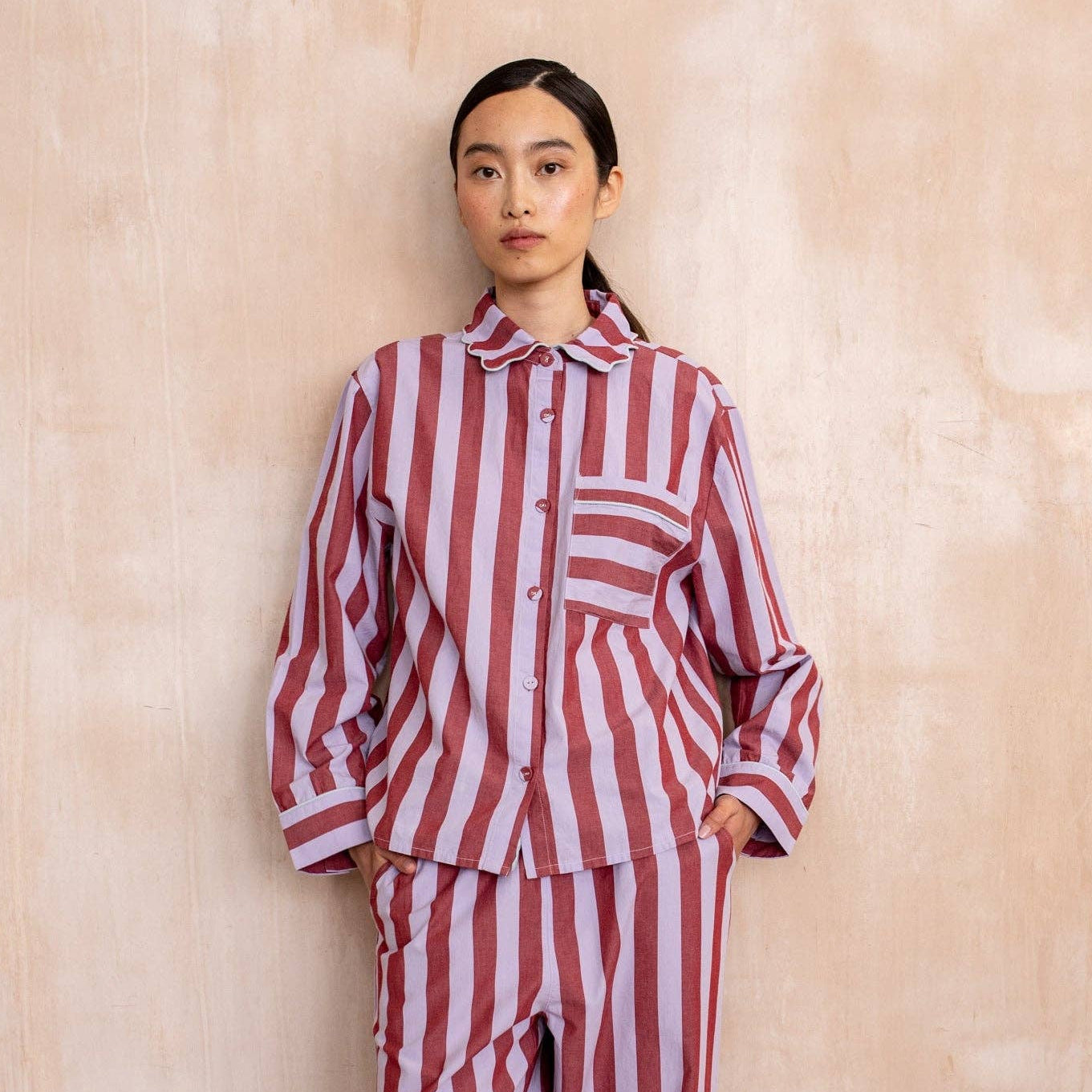 Person wearing a red and lilac striped outfit against a beige background