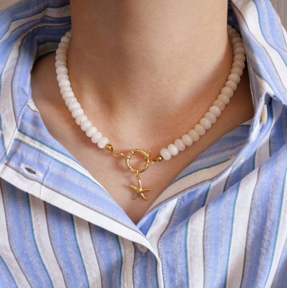 Necklace with a gold clasp and star charm worn by a person in a blue and white striped shirt.