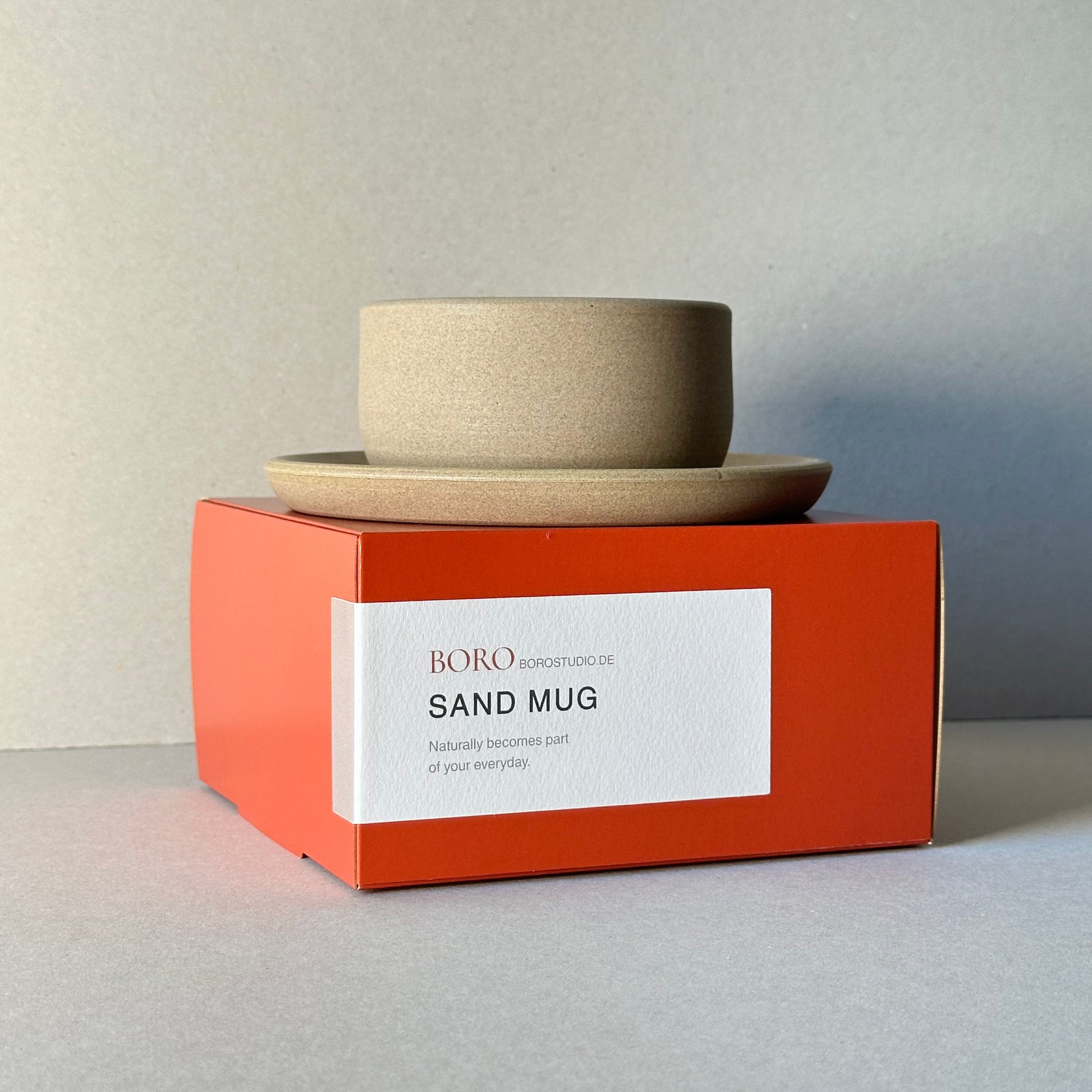 Sand mug packaging with a white label on an orange box against a gray background