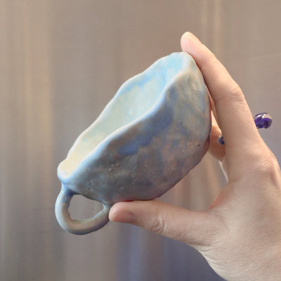 The Big Sea Cup - sea foam blue and creme glazed ceramic tea cup, held in a hand against a steel grey background