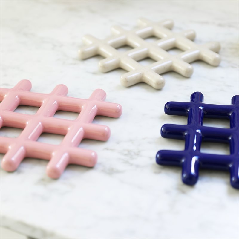 stoneware trivets in a modern grid shape with shiny glazes in multiple colours: cream, pink and royal blue on a marble counter top